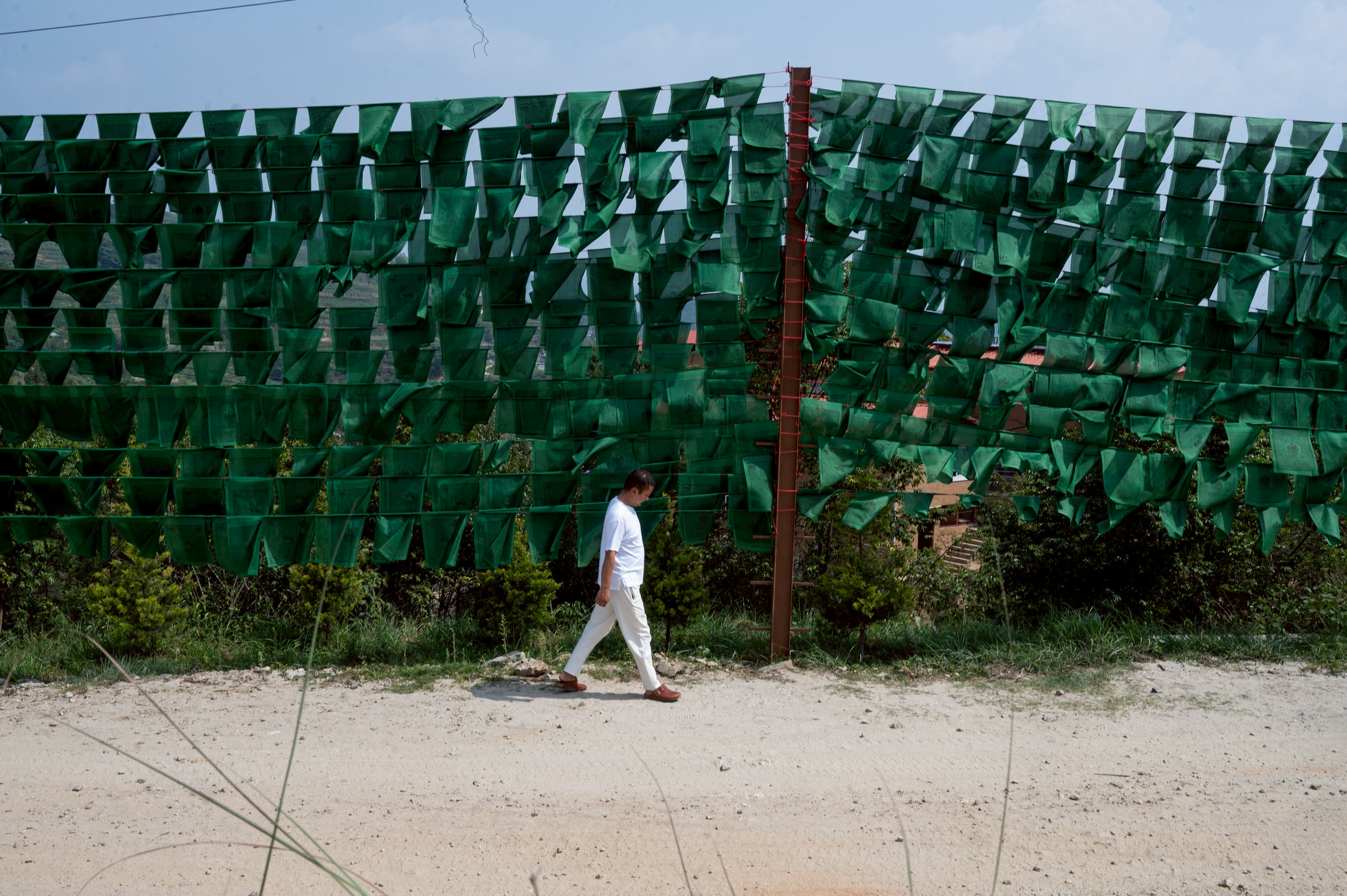 仁波切獨行在山門口。一旁的是整片的綠色風馬旗。(攝影_林彥廷)